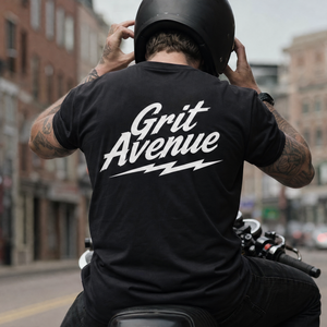 Person wearing a black 'Grit Avenue' t-shirt on a motorcycle in an urban setting.